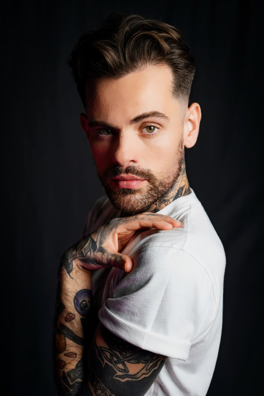 White man with tattoos in a white t-shirt looking over his shoulder