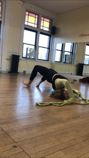 Person in dance studio lays on back with knees raised, fabric above head