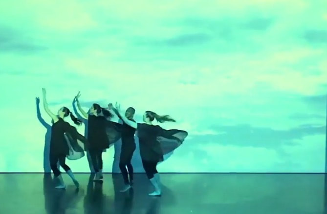 Four dancers on stage, Sheer black fabric flowing out Amid sea green screen