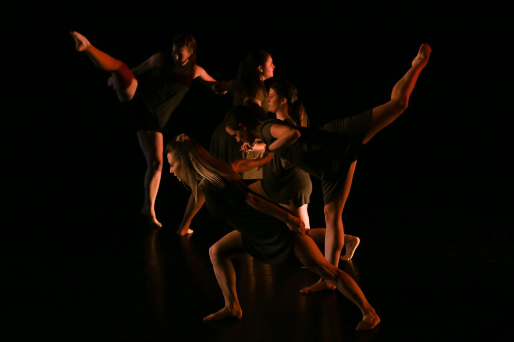 Five dancers in line, Holding hands, two legs extend,  Wearing olive green