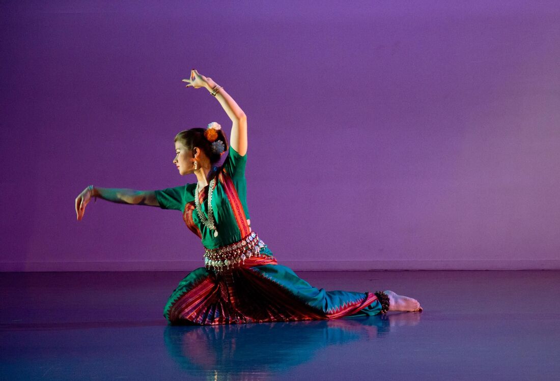 Purple light behind Dancer wears Indian clothes On knees, one arm up