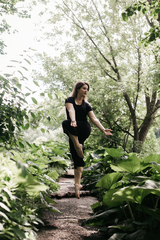 White woman jumping Along a path in the woods Her arms to the right