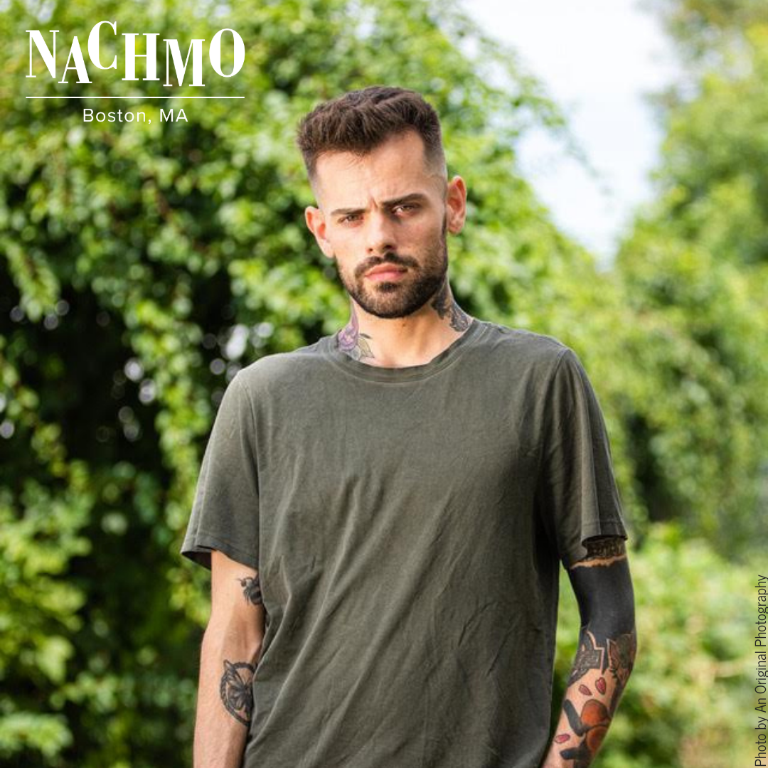 White man with tattoos
Standing outside by bushes
In shorts and a tee