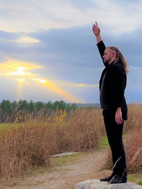 Christopher standing with his arm raised in the air in a large field