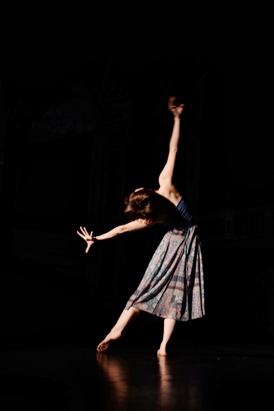 Dancer in long skirt Arms stretched, one foot points on floor  Facing to the back
