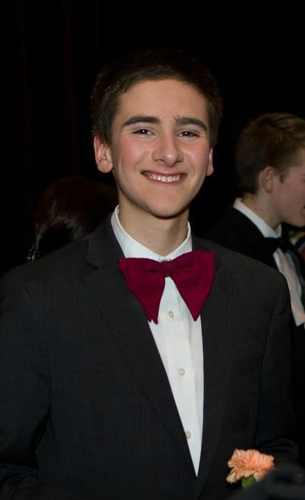A teenage boys stands Wears jacket and red bow tie Smiles at camera