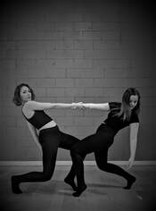 Black and white photo, Two dancers hold hands, lean back In front of brick wall 