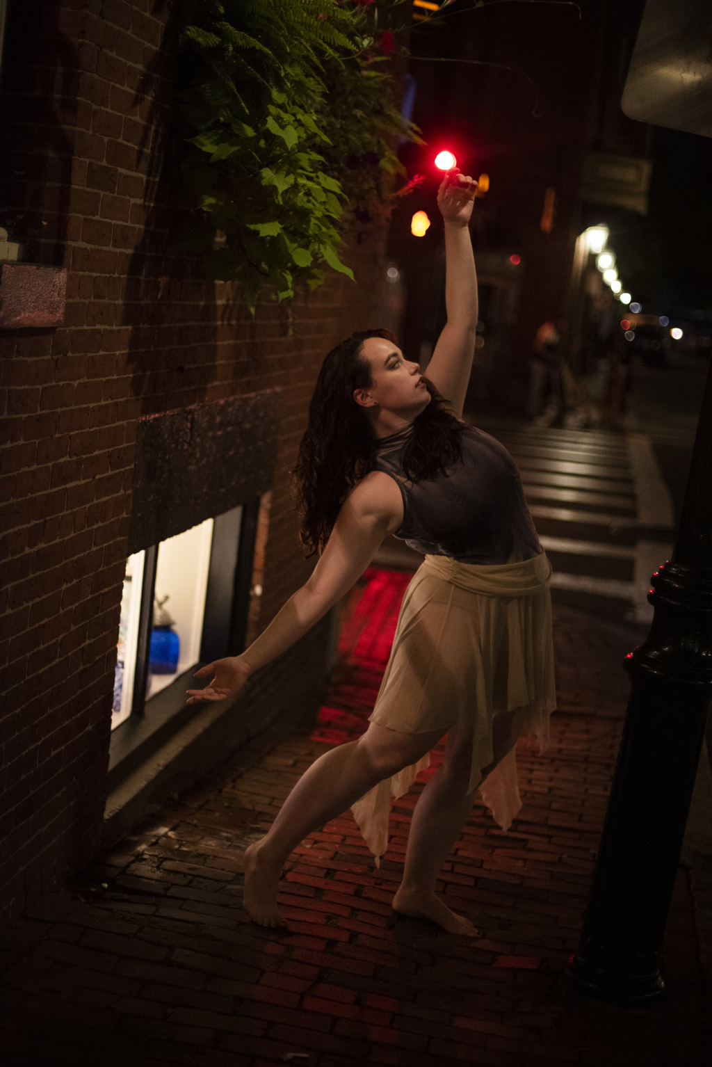 White woman arms outStanding in the brick lined streetRed light behind her