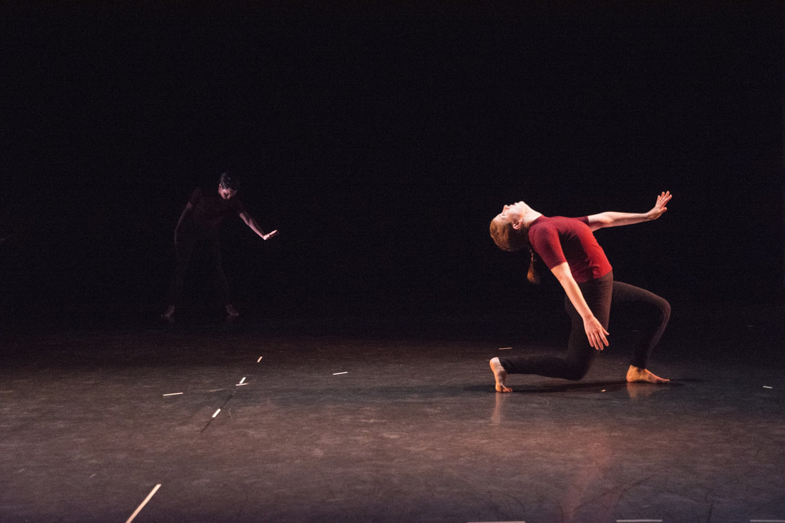 Two dancers on stage, One in all black, one red shirt, Arms pushing out