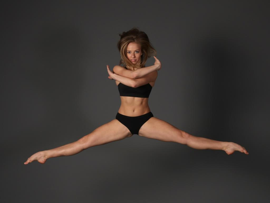 Woman in split jump Arms crossed, wearing black bra top Black shorts, hair flying
