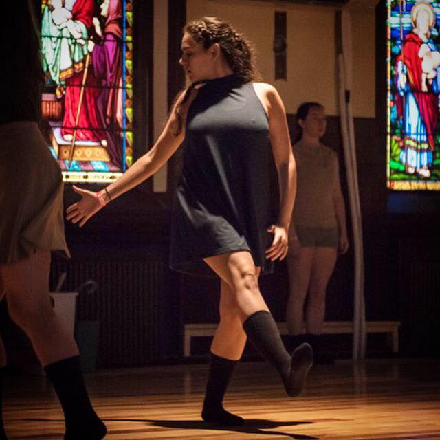 Dancer in all black Foot in front, looks at back hand By stained glass windows