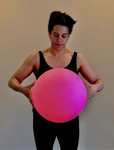 Black woman in black Holding a large bright pink ball Before a white wall