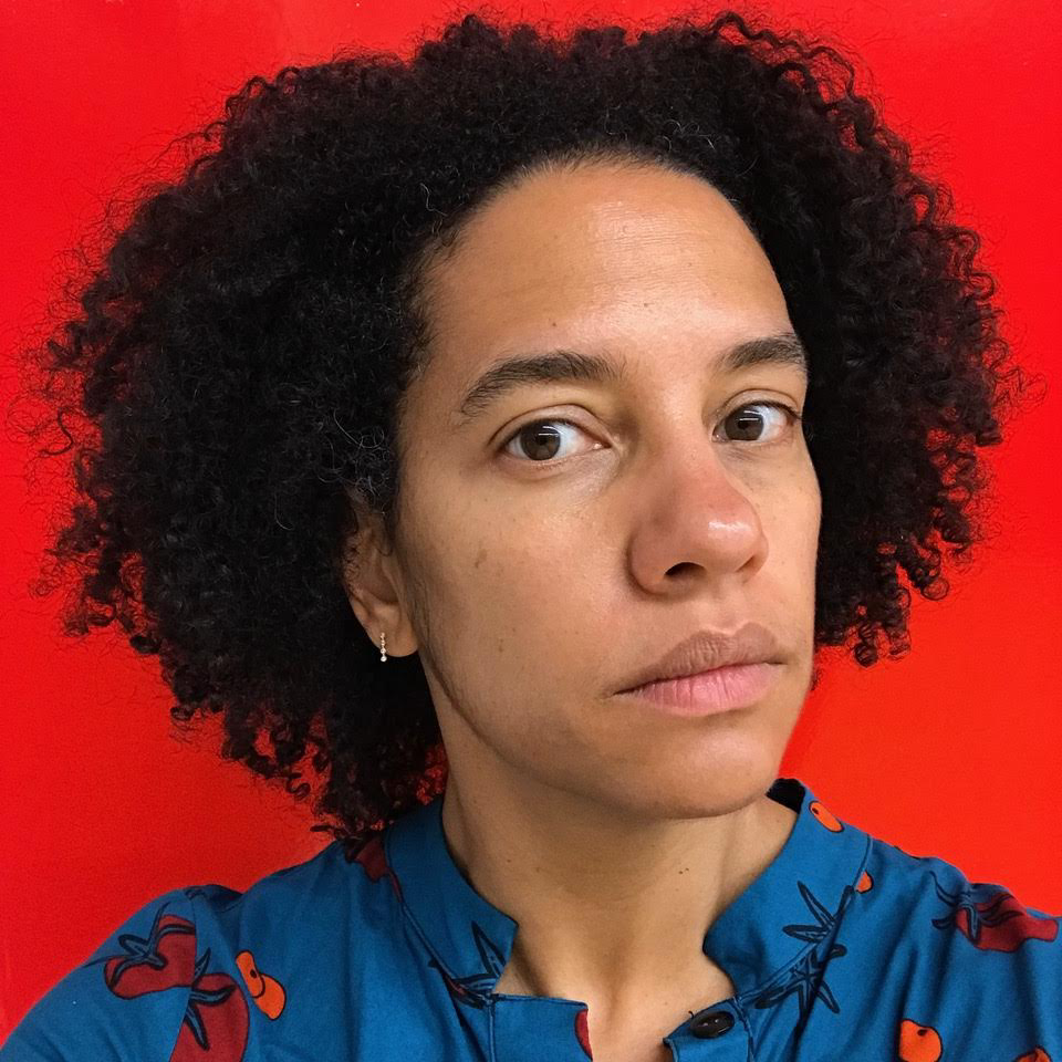 Black woman in blueIn front of a bright red wallMaking eye contact