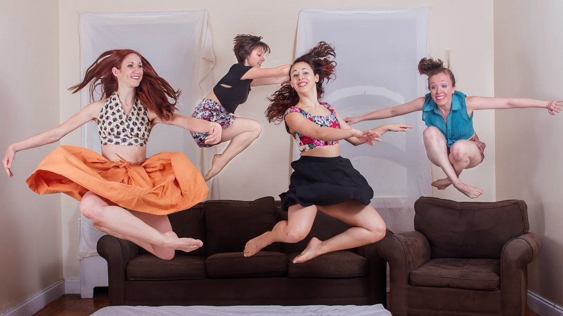 Four dancers jumping In front of brown couches they All smile hair flowing