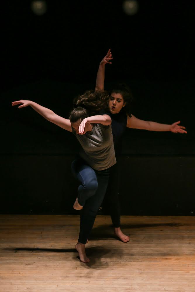 Two women dancing White arms and legs extended From dark colored clothes