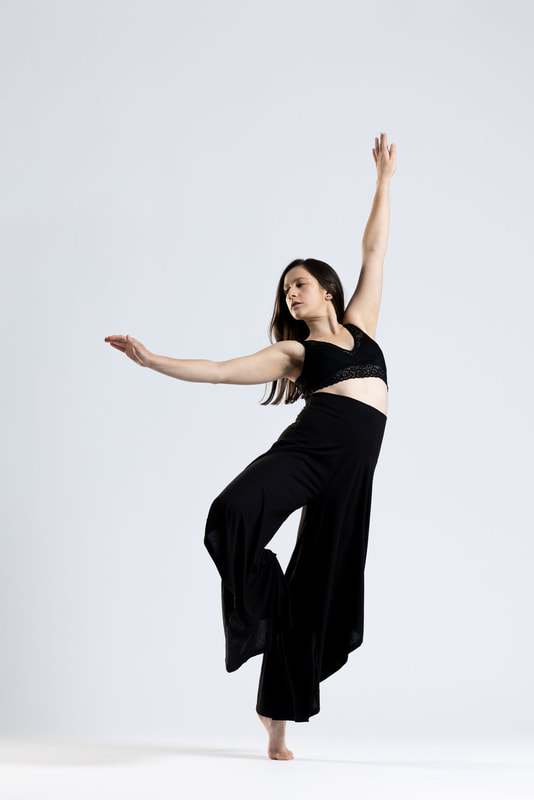 Marissa stands on one leg with arms outstretched, leaning as if about to fall off center. 