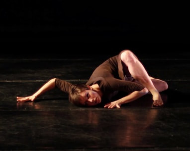 Dancer on black floor Head on floor, elbows in air One leg crossed over