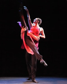 Dancer in red dress,  Person behind lifts, legs split,  Looking up at arm