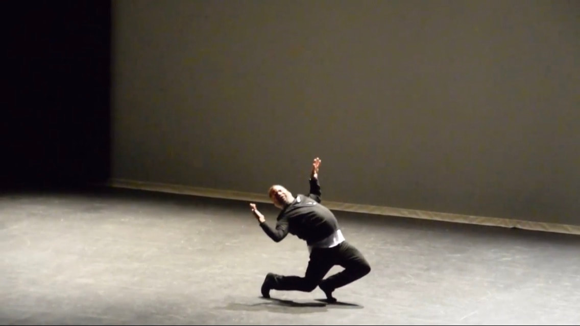Dancer on a stage Knees bent, back arched, bent arms out Wearing all black clothes