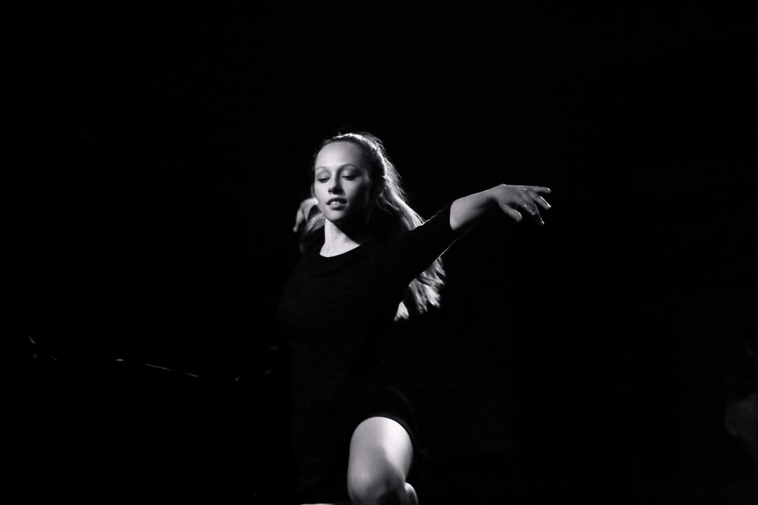 Black and white photo Woman dances in black room Arms out, one knee bent