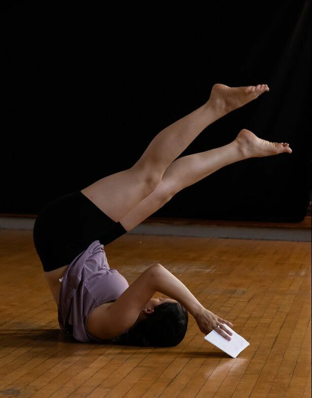 Dancer on wood floor Rolls on shoulders, legs in air Holding white paper