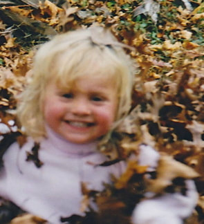 A young blonde child Smiles while playing in fall  Leaves are all around