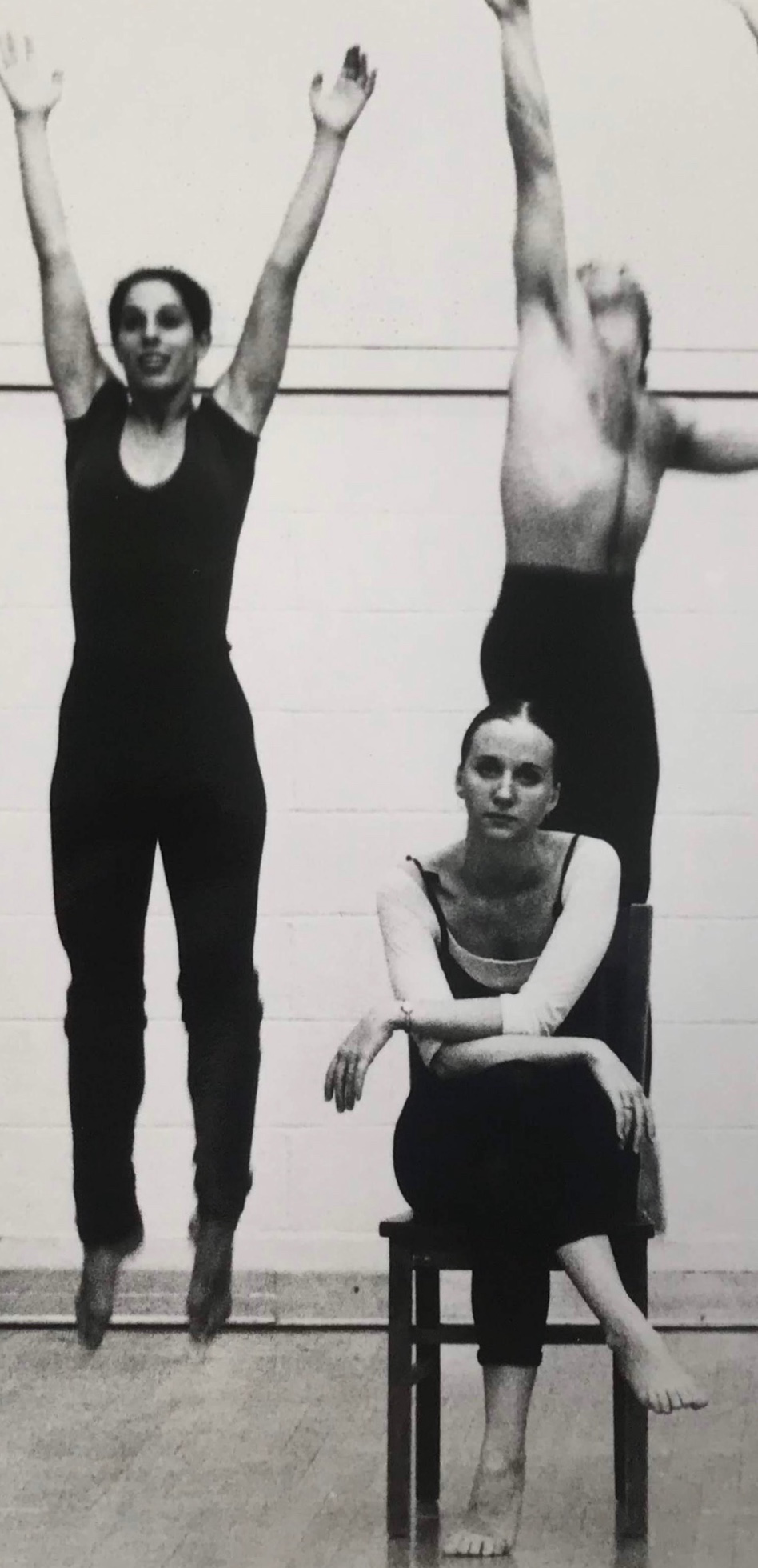 Three dancers in black One on chair, two jump behind Black and white photo 