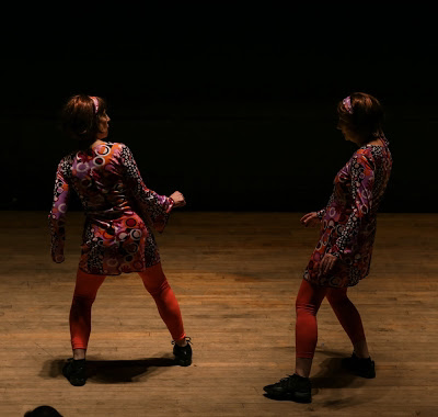 Two dancers on stage Wear bright, colorful dresses  With wigs on their heads 