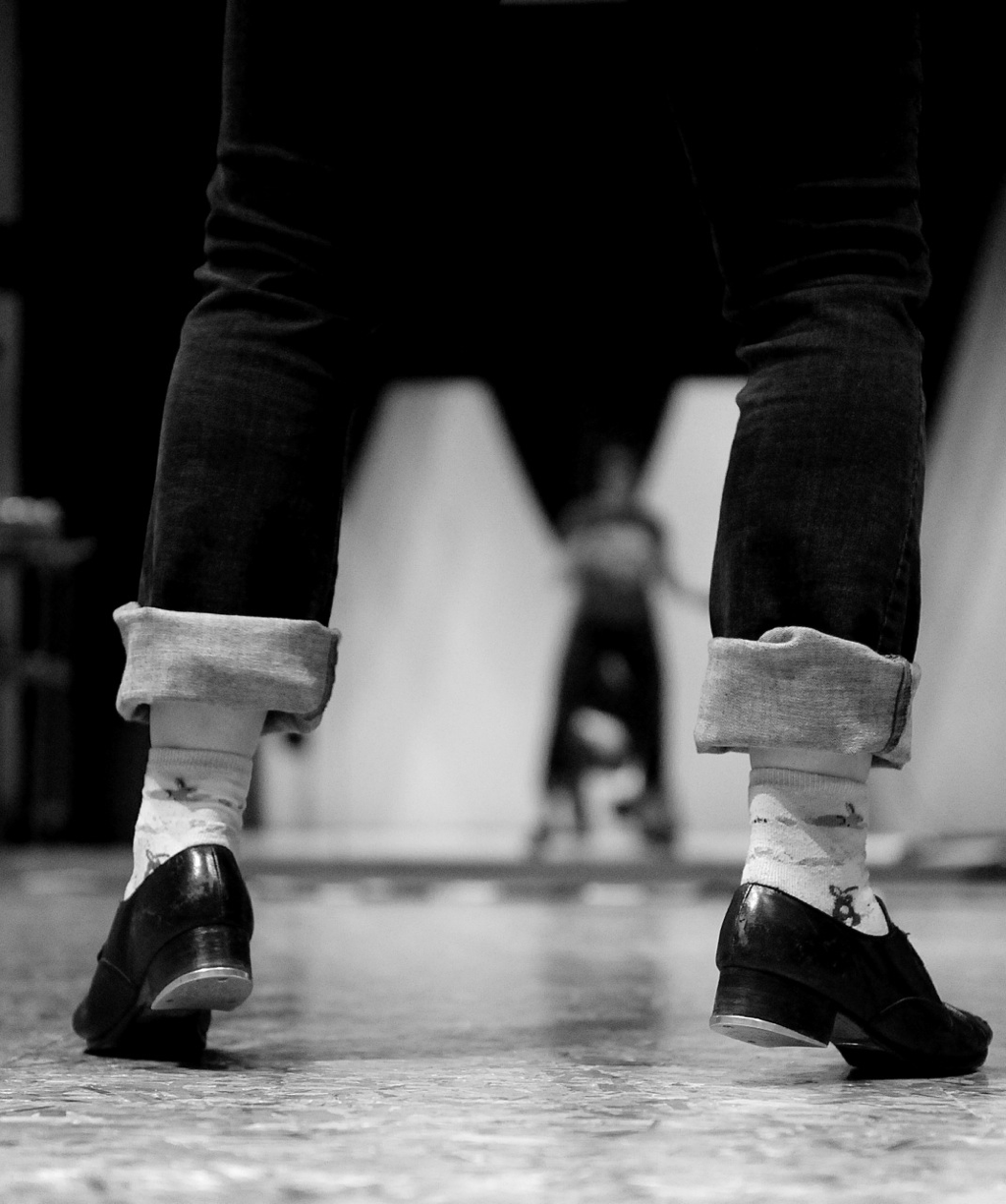 Black and white photo Black tap shoes facing away  Dark pants cuffed, white socks