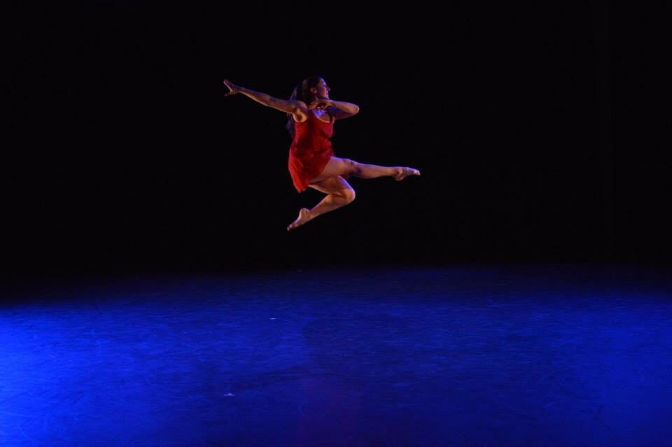 White woman jumping in a red dress and blue light