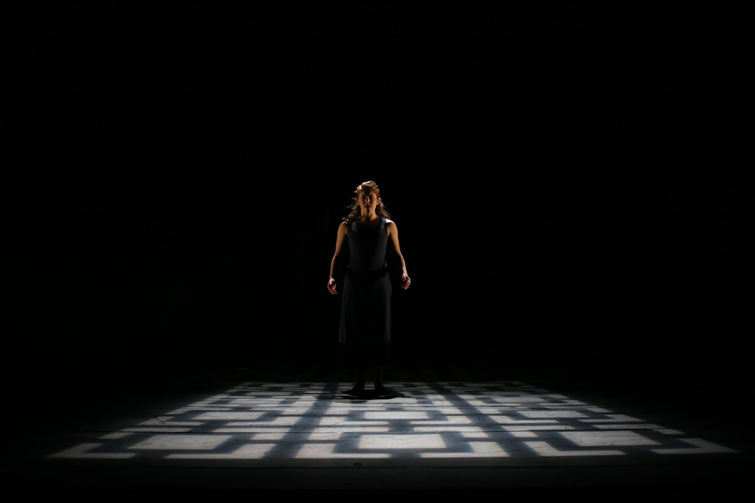 Wearing all black clothes Woman stands downstage center Lights make squares on ground